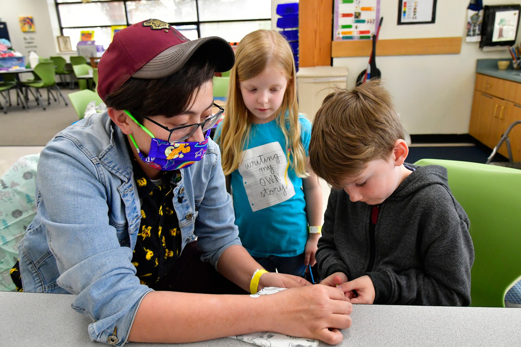 Kayla Hoffmann, left, Training and Curriculum Specialist, and Bethany Powell, center, watch as David Warren pins mask material to a pattern.
