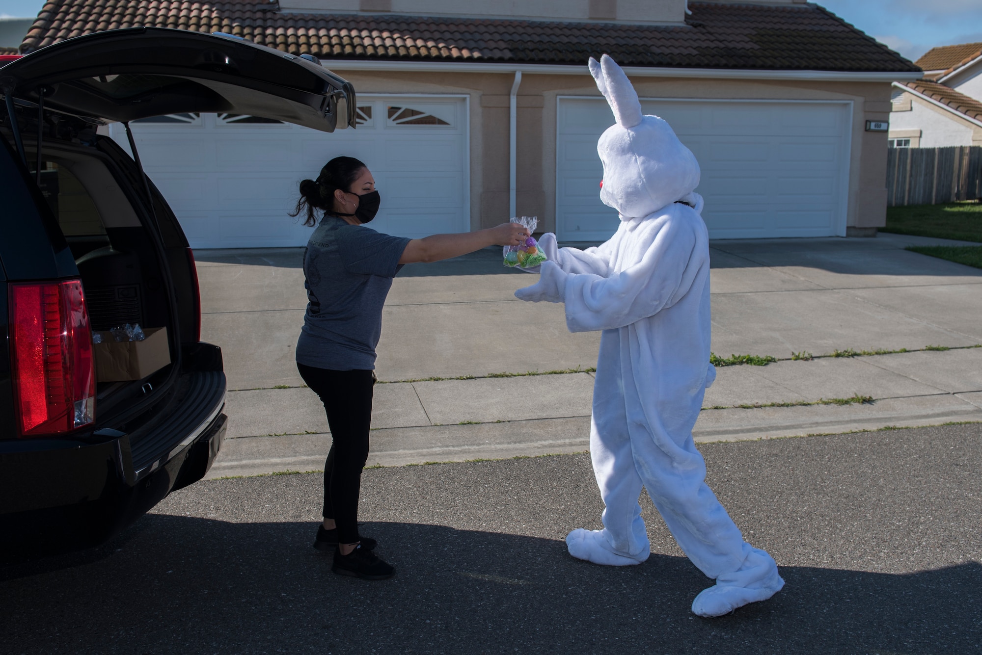 Jannet Rodriguez, 60th Security Forces Squadron unit program coordinator, hands candy to the Easter Bunny April 11, 2020, at Travis Air Force Base, California. Rodriguez asked the Easter bunny to visit children with deployed parents, so the children could still enjoy Easter while sheltering at home. (U.S. Air Force photo by Airman 1st Class Cameron Otte)