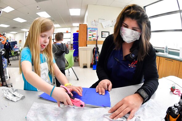 Bethany Powell, left, cuts out mask material using a pattern with direction from Sandra Edelman.