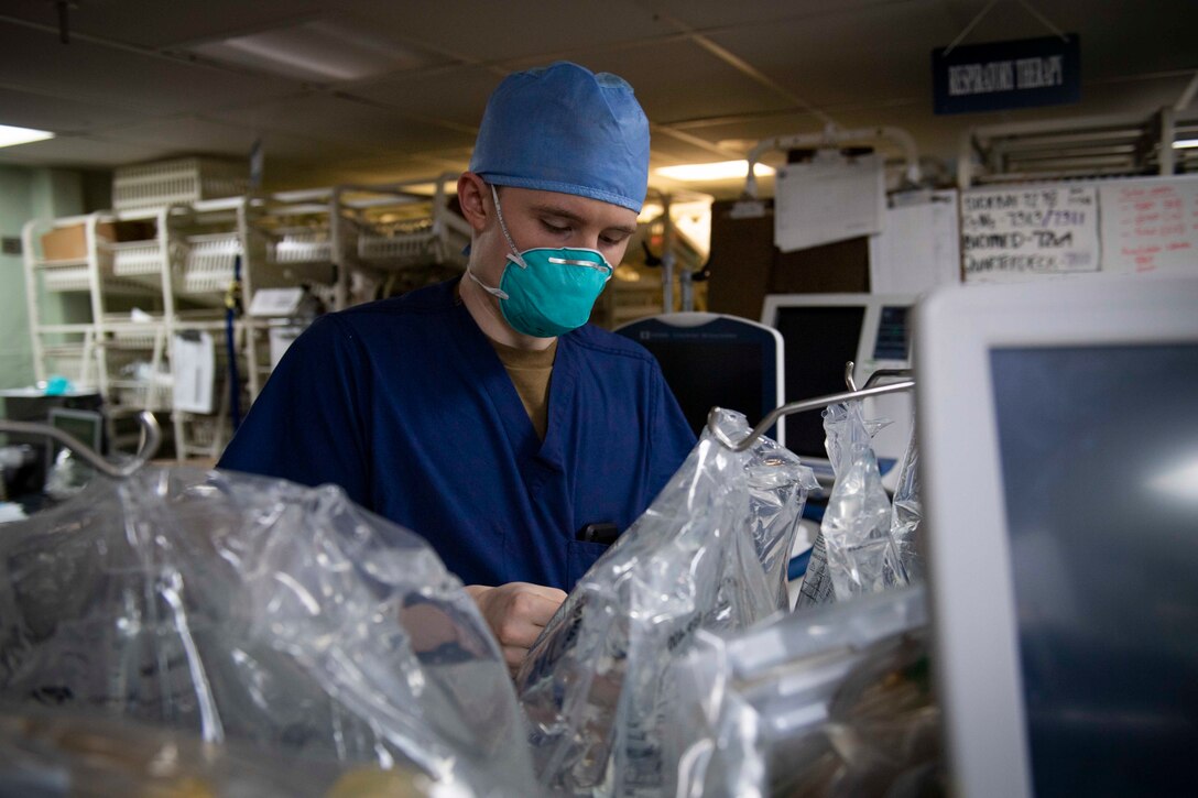 A man in hospital scrubs and wearing a mask configures medical equipment.