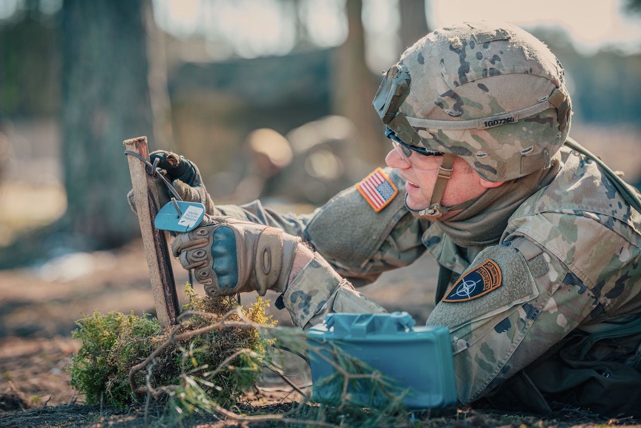 Soldier lies on the dirt to set up a claymore mine.