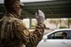 An Airman in uniform, wearing a mask and gloves duet to COVID-19 safety precautions, waves on vehicles in line to pick up pizzas in a parking lot.