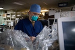 A man in hospital scrubs and wearing a mask configures medical equipment.