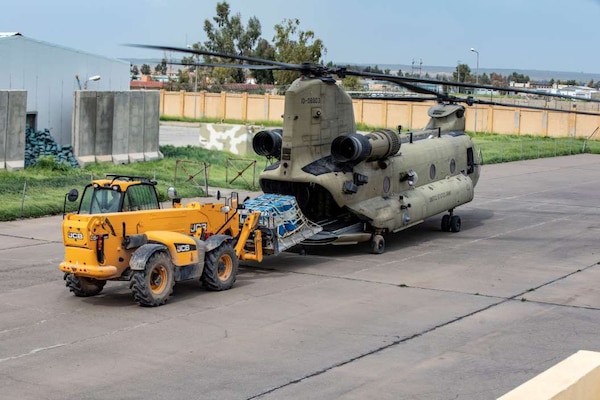 A small vehicle loads a pallet onto a helicopter.