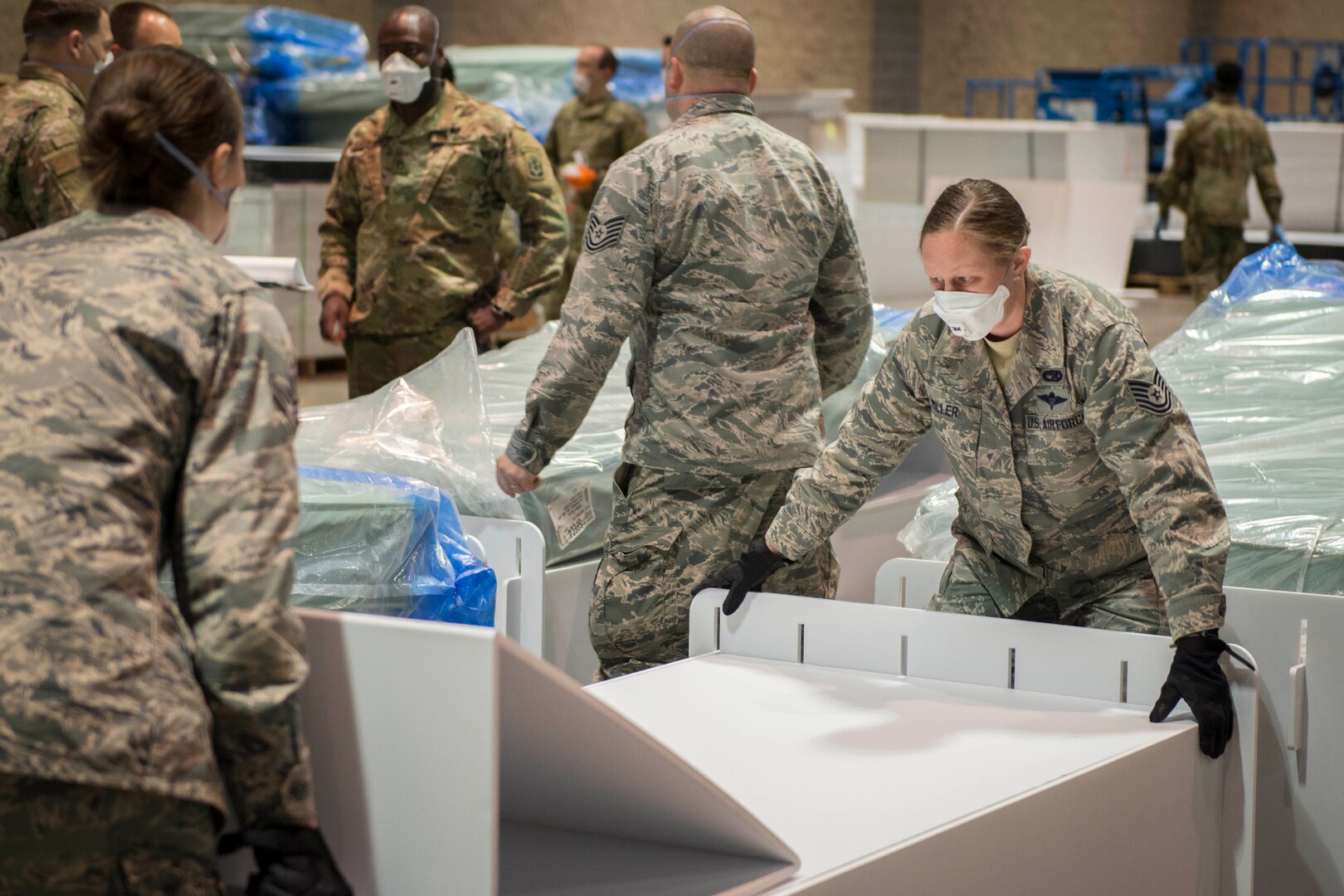 Service members work together to assemble equipment in a large indoor area.