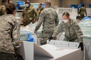 Service members work together to assemble equipment in a large indoor area.