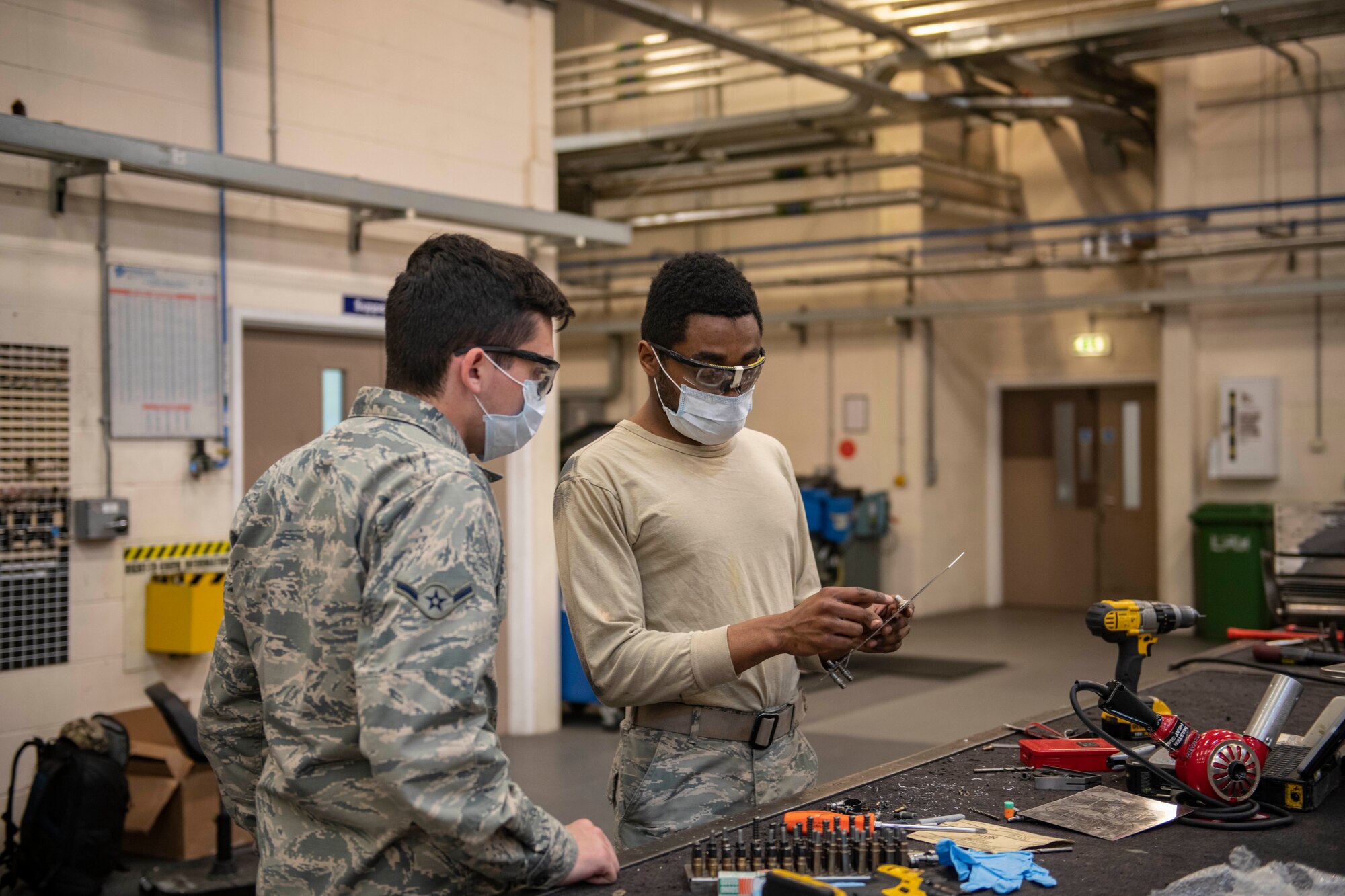 Airman 1st Class Jevaughn Harvey, 100th Maintenance aircraft structural maintenance apprentice, trains Airman Gavin Walker, 100th MXS aircraft structural maintenance apprentice, on taking stuck screws out of a piece of metal, at RAF Mildenhall, England, April 8, 2020. The 100th MXS aircraft structural maintenance shop preserves and extends the life of components for all Team Mildenhall airframes. (U.S. Air Force photo by Staff Sgt. Luke Milano)