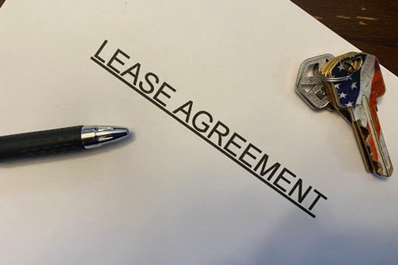 A photograph shows two keys, a pen and a paper with the words lease agreement.