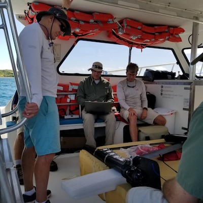 The U.S. Army Engineer and Development Center’s Justin Wilkens, a research biologist with the Environmental Laboratory, checks the waypoints using the SubSeaSail’s G6 navigation software on his laptop. The unmanned surface vessel was taken to Vieques, an island off the coast of Puerto Rico, for a demonstration by Wilkens and a team of ERDC-EL research biologists, including Dr. Guilherme Lotufo and Dr. Mark Ballentine. The USV gathered data indicating the presence of munitions constituents from unexploded underwater ordnance, a problem at sites around the world. Chris Todter, far left, a SubSeaSail partner, and Tom Goddard, far right, SubSeaSail Fabrication and Testing, are also visible in the photo.