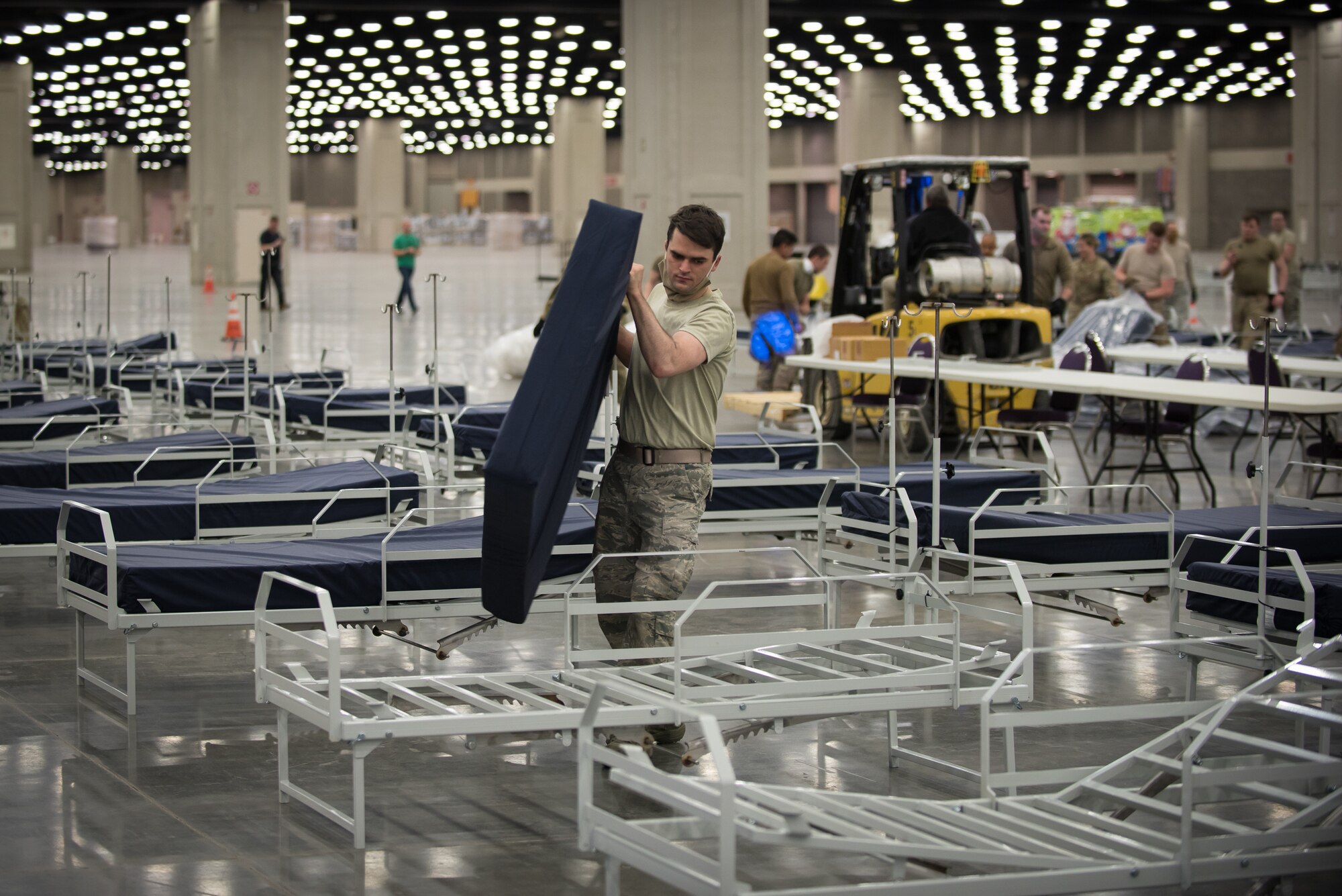 Senior Airman Tristan Baxter of the Kentucky Air National Guard's 123rd Civil Engineer Squadron places a mattress on a hospital bed at the Kentucky Fair and Exposition Center in Louisville, Ky., April 11, 2020. The site, which is expected to be operational April 15, will serve as an Alternate Care Facility for patients suffering from COVID-19 if area hospitals exceed available capacity. The location initially can treat up to 288 patients and is scalable to 2,000 beds. (U.S. Air National Guard photo by Dale Greer)