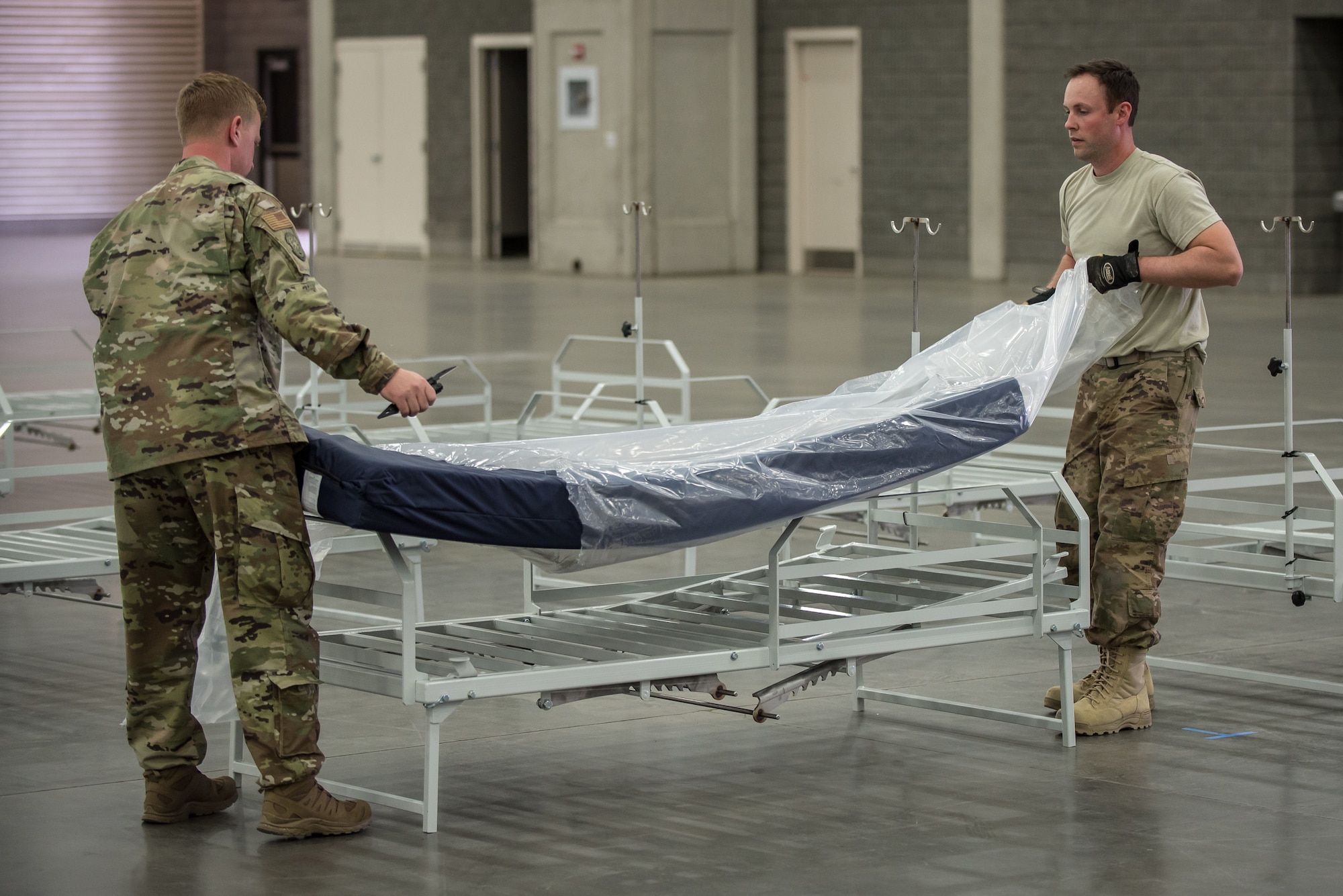 Capt. Jason Selby (left) and Staff Sgt. Wesley Hack of the Kentucky Air National Guard's 123rd Civil Engineer Squadron place a mattress on a hospital bed at the Kentucky Fair and Exposition Center in Louisville, Ky., April 11, 2020. The site, which is expected to be operational April 15, will serve as an Alternate Care Facility for patients suffering from COVID-19 if area hospitals exceed available capacity. The location initially can treat up to 288 patients and is scalable to 2,000 beds. (U.S. Air National Guard photo by Dale Greer)