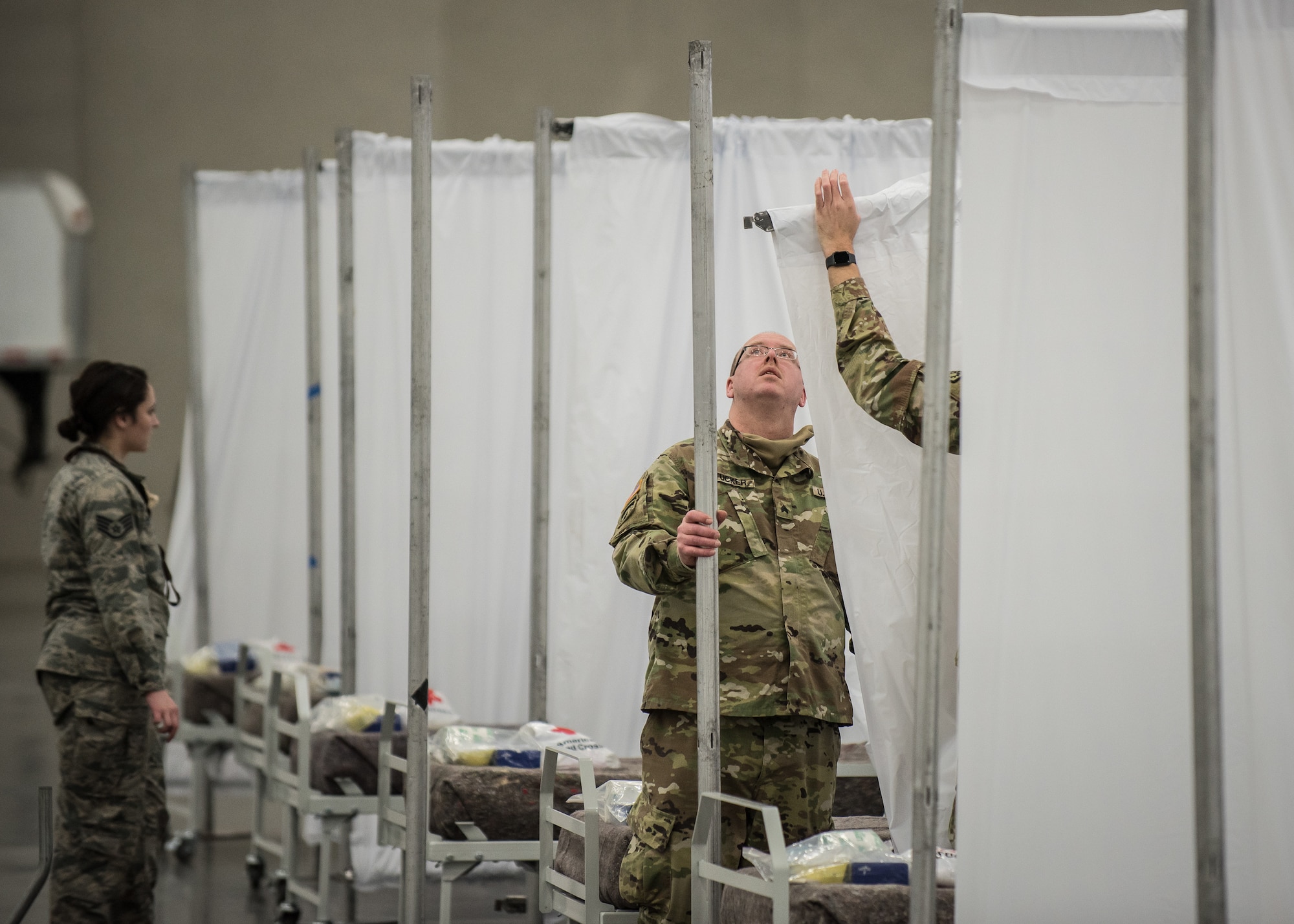 Soldiers from the Kentucky Army National Guard’s 103rd Chemical Battalion set up vinyl partitions to go between hospital beds at the Kentucky Fair and Exposition Center in Louisville, Ky., April 14, 2020. The site, which is expected to be operational April 15, will serve as an Alternate Care Facility for patients suffering from COVID-19 if area hospitals exceed available capacity. The location initially can treat up to 288 patients and is scalable to 2,000 beds. (U.S. Air National Guard photo by Dale Greer)