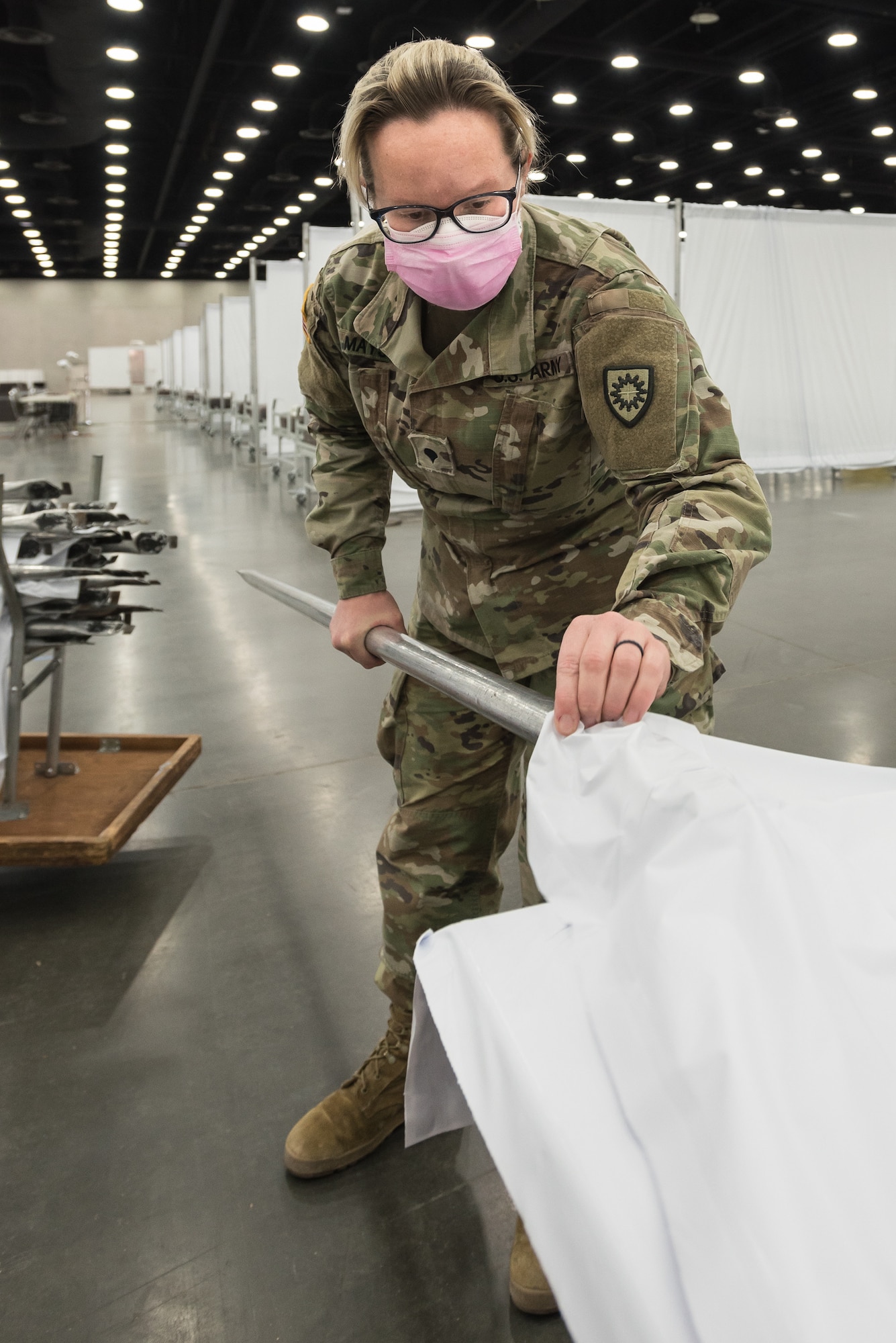 Spc. Samantha Mays of the Kentucky Army National Guard’s 103rd Chemical Battalion sets up vinyl partitions to go between hospital beds at the Kentucky Fair and Exposition Center in Louisville, Ky., April 14, 2020. The site, which is expected to be operational April 15, will serve as an Alternate Care Facility for patients suffering from COVID-19 if area hospitals exceed available capacity. The location initially can treat up to 288 patients and is scalable to 2,000 beds. (U.S. Air National Guard photo by Dale Greer)