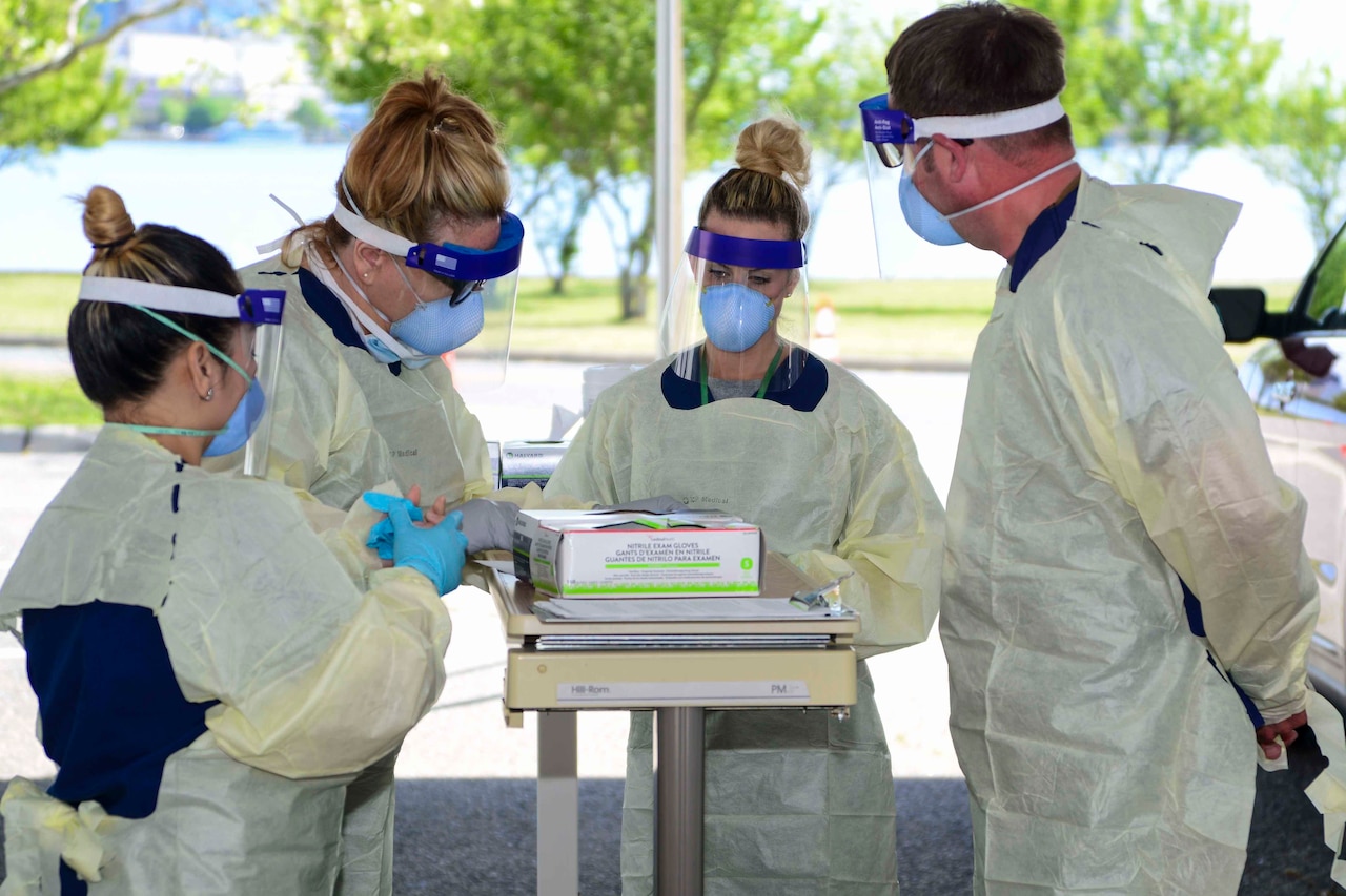 Three women and a man wearing protective gear put on their gloves.