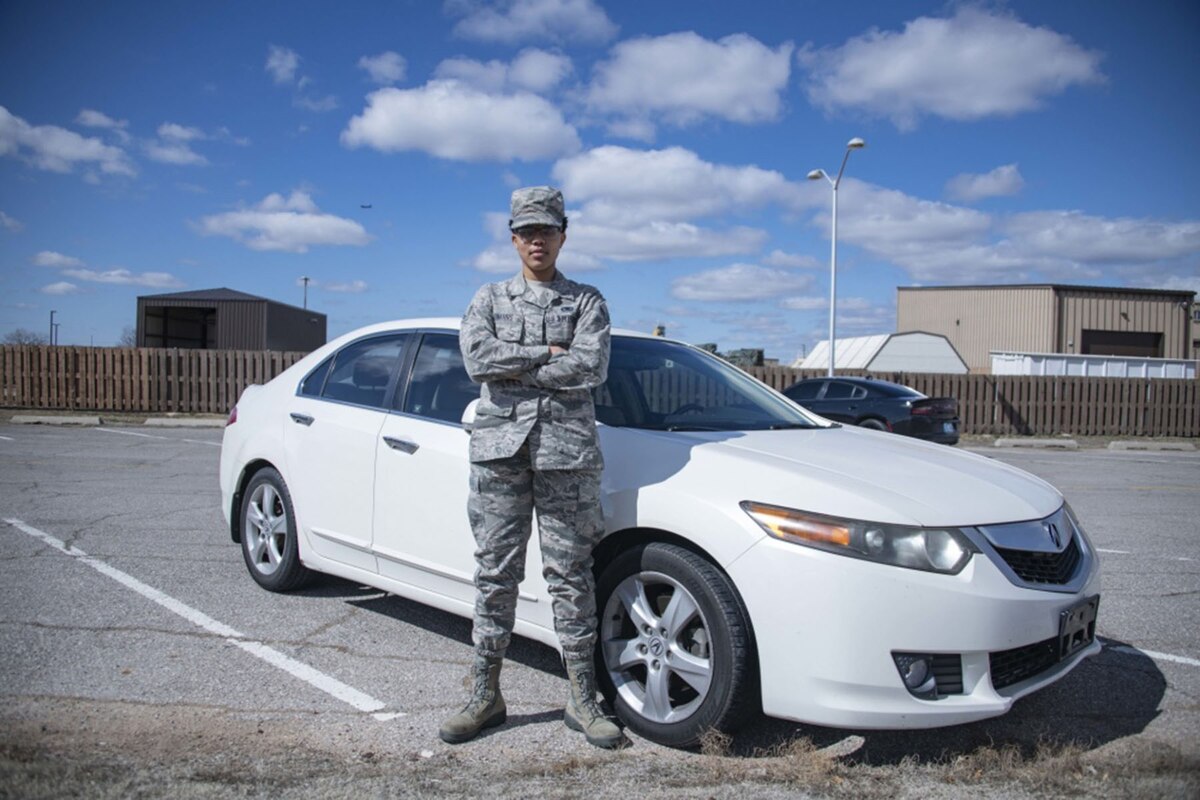 A woman in a military uniform stands in front of a car.