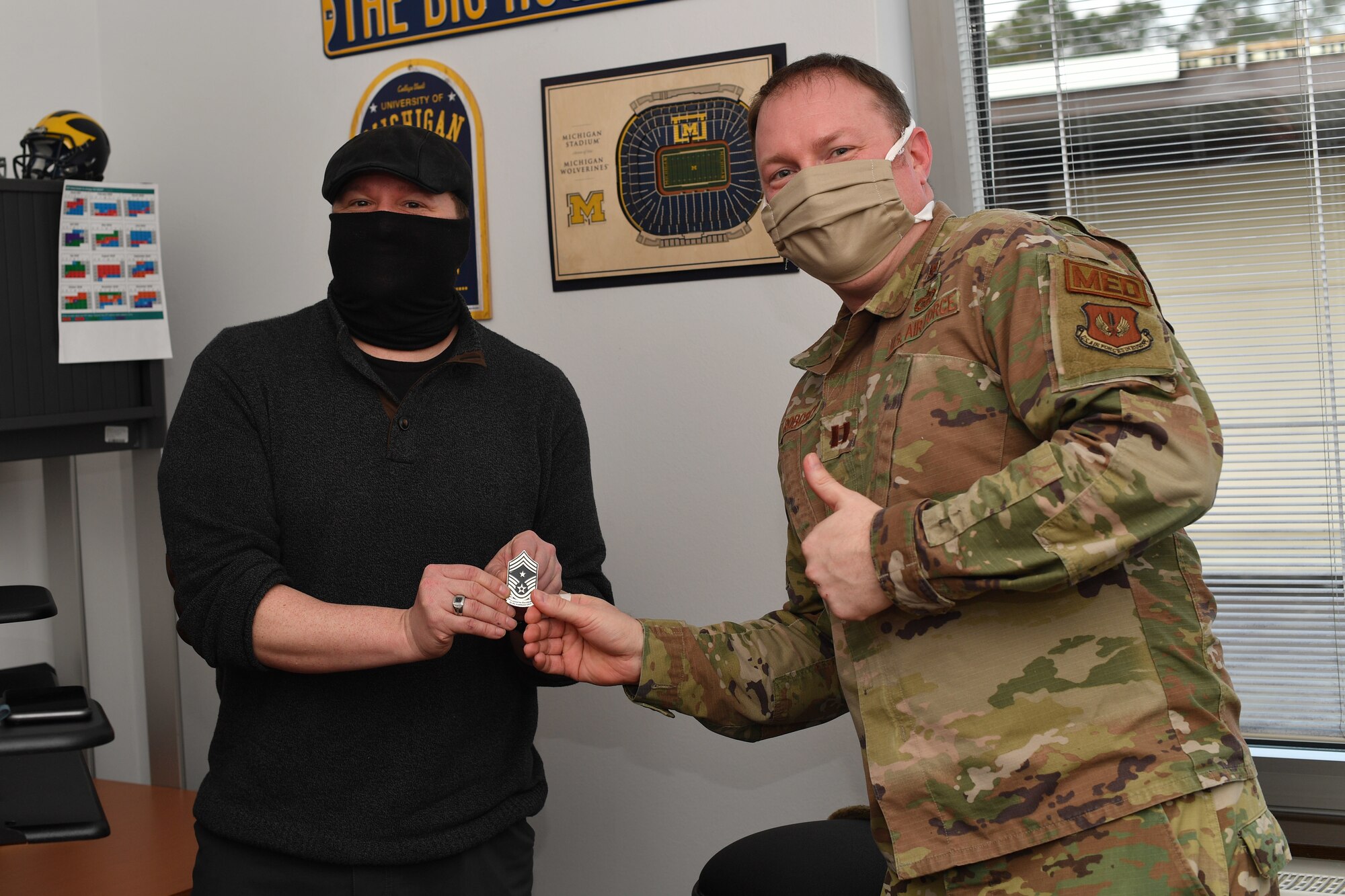 Two Airmen holding a coin pose for a photo in an office.