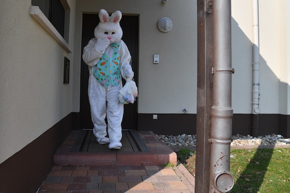 The Easter Bunny walks away from a house holding Easter bags.
