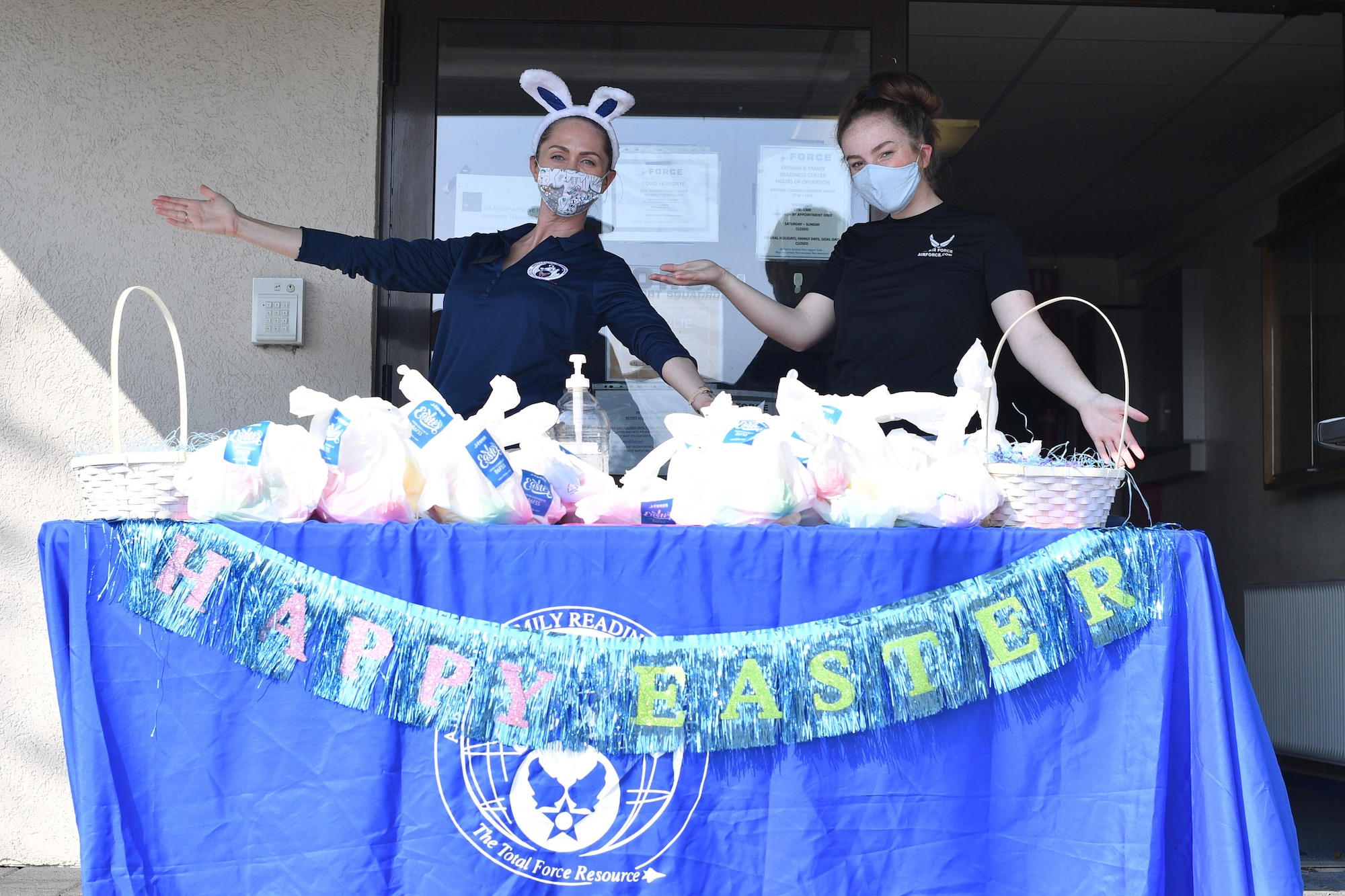 Two individuals stand behind a table filled with Easter bags.