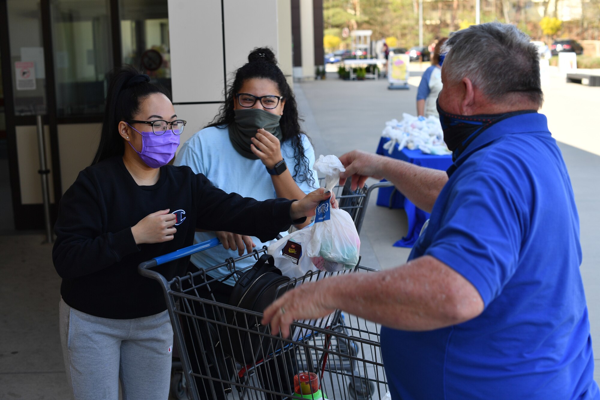 An individual hands an Easter bag to two shoppers leaving the commissary.