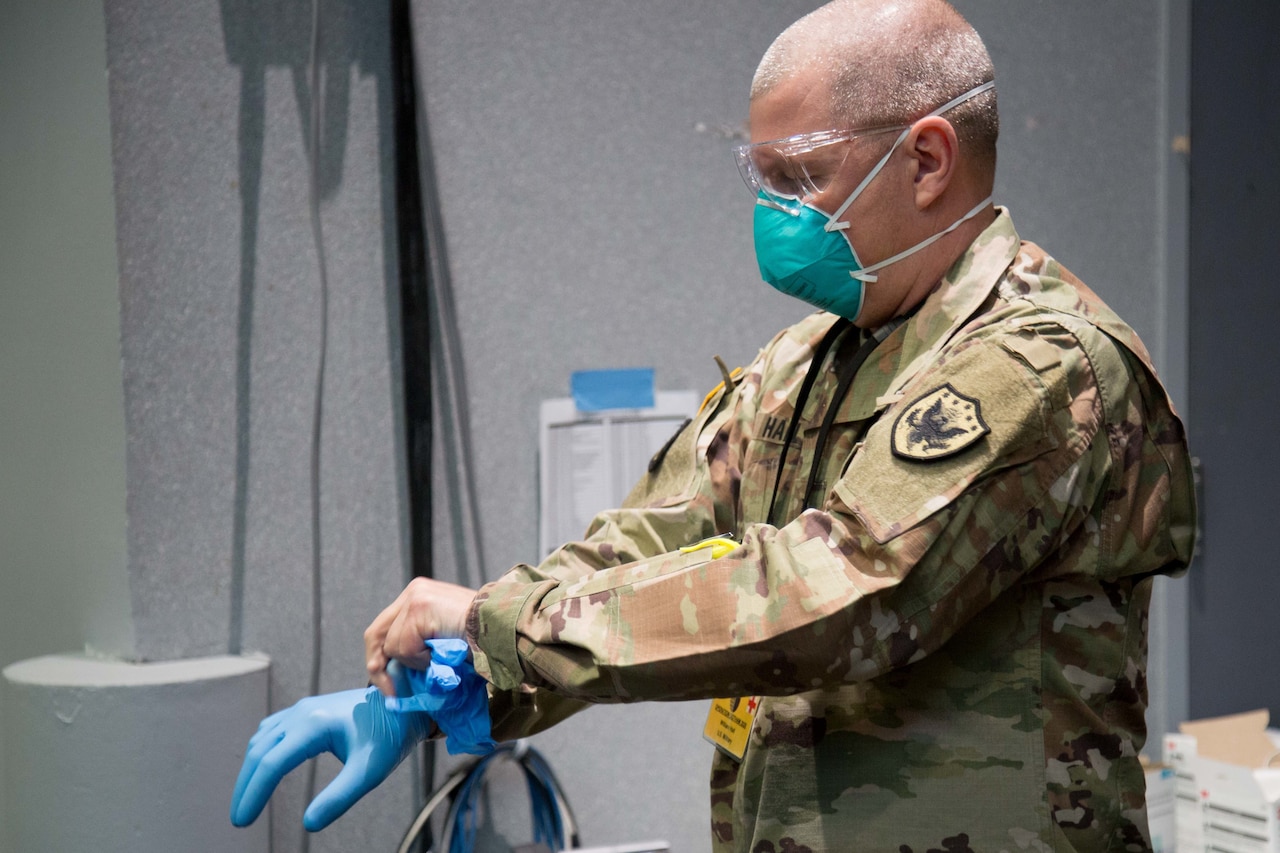 An Army general wearing eye protection and a blue face puts on a pair of blue latex gloves.