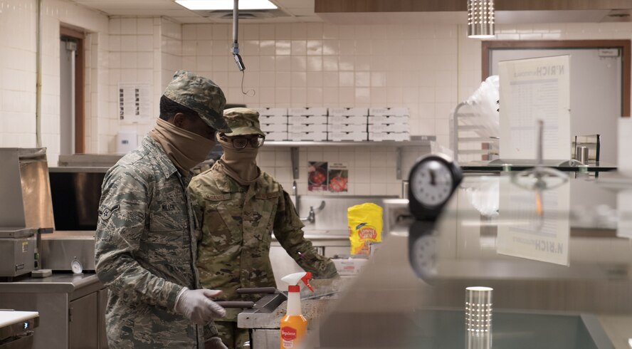 Airman Tony Miller, 2nd Force Support Squadron dining facility shift worker, cooks a burger for a customer as Airman 1st Class Jordan McDaniel, 2nd FSS DFAC shift worker, stands by at Barksdale Air Force Base, La., April 15, 2020. All food items are currently being made to go. (U.S. Air Force photo by Tech. Sgt. Daniel Martinez)