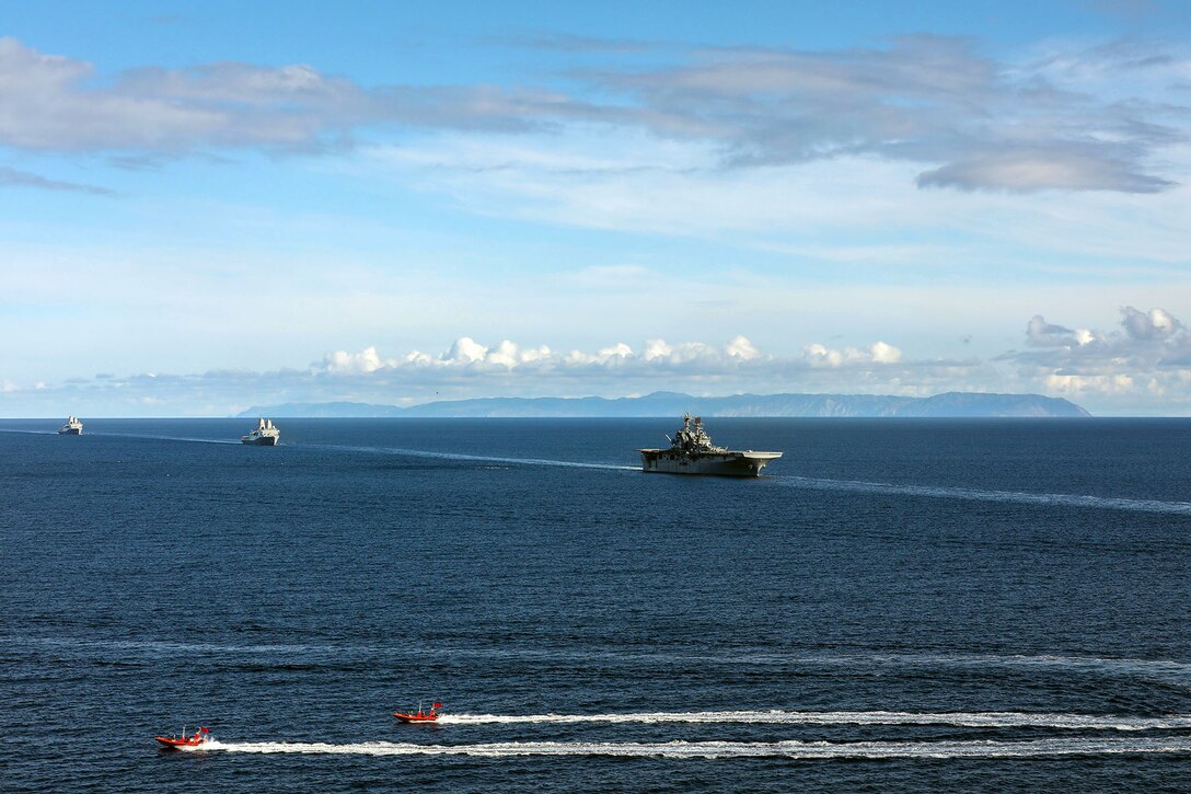 A large ship moves through the water in line with two other ships while two smaller boats are in the foreground.