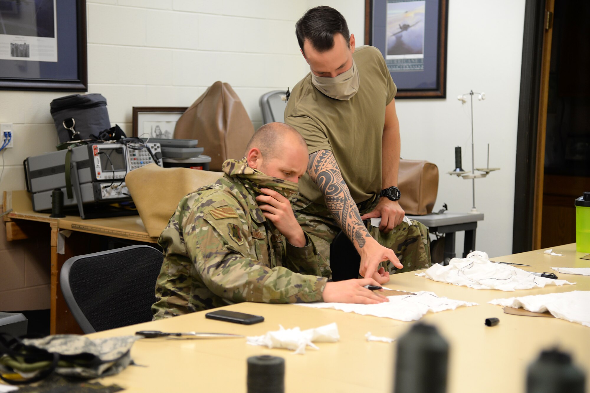 A picture of U.S. Air Force Senior Airman Michael R. Ottaviano, and Staff Sgt. Brandon M. Staines, aircraft ordinance maintenance technology (Egress) technicians, volunteering to prepare fabric for face masks.