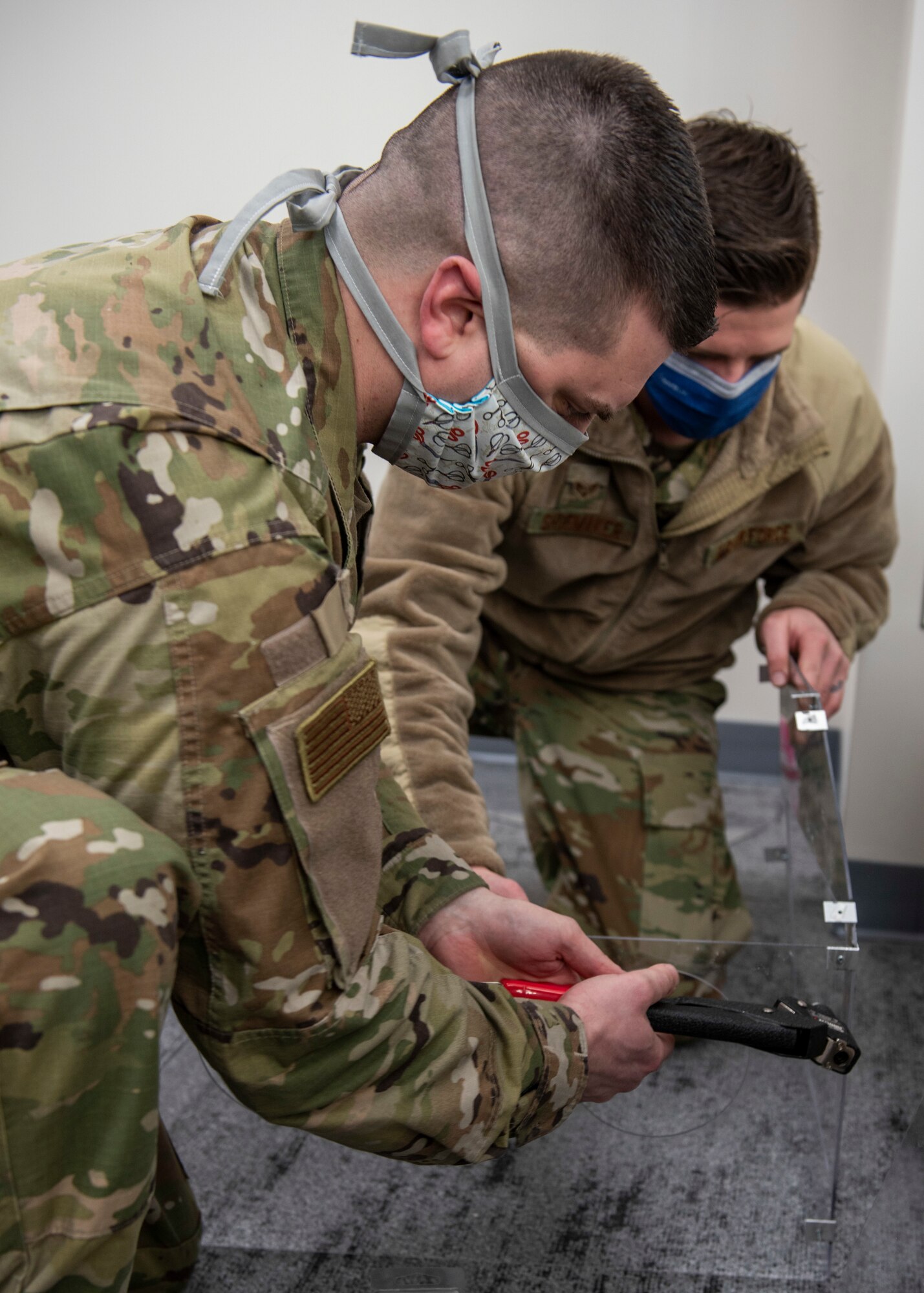 U.S. Air Force Staff Sgt. Andrew Taylor, 673d Medical Support Squadron medical logistics noncommissioned officer in charge of acquisitions, attaches a rivet to a plastic polycarbonate enclosure while U.S. Air Force Senior Airman Michael Shoemaker, 673d Medical Support Squadron biomedical equipment technician, holds the enclosure steady at Joint Base Elmendorf-Richardson, Alaska, April 7, 2020. Taylor and Shoemaker designed and built the reusable device to be a protective barrier between medical providers and a patient to prevent possible exposure to COVID-19 and other airborne diseases. The innovated enclosure can be placed over a patient’s head and upper torso prior to intubation or similar treatments, with access to the patient via two holes at the head of the enclosure for a physician's hands and arms, and two side doors for additional access.