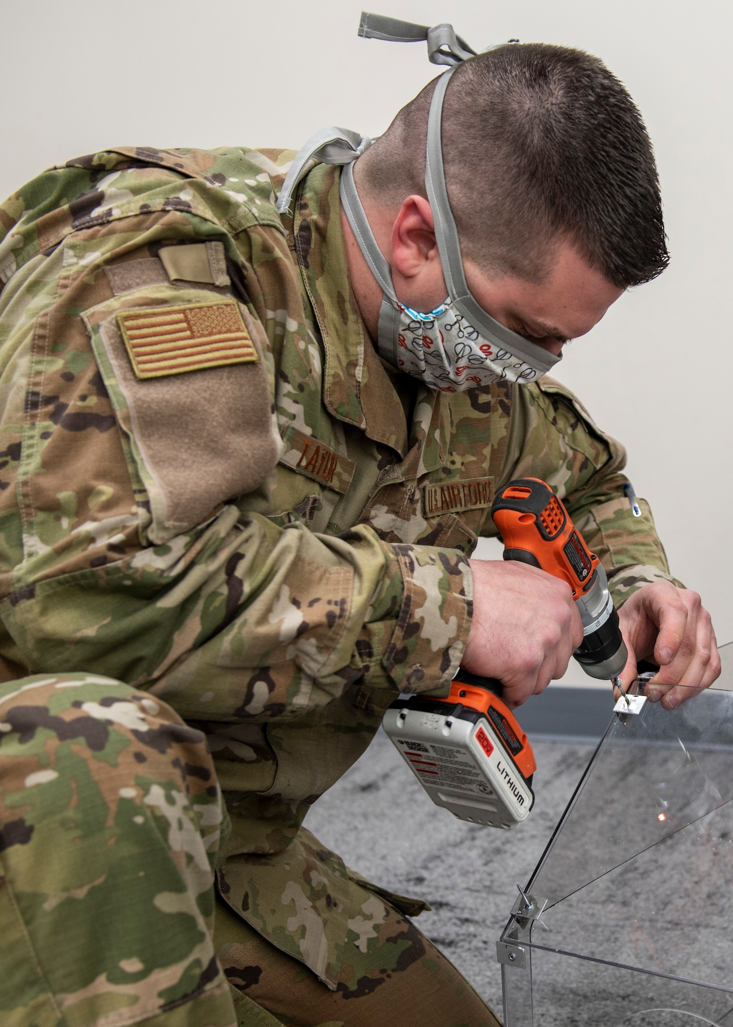 U.S. Air Force Staff Sgt. Andrew Taylor, 673d Medical Support Squadron medical logistics noncommissioned officer in charge of acquisitions, drills a hole in a plastic polycarbonate enclosure at Joint Base Elmendorf-Richardson, Alaska, April 7, 2020. Taylor and U.S. Air Force Senior Airman Michael Shoemaker, 673d Medical Support Squadron biomedical equipment technician, designed and built the reusable device to be a protective barrier between medical providers and a patient to prevent possible exposure to COVID-19 and other airborne diseases. The enclosure can be placed over a patient’s head and upper torso prior to intubation or similar treatments, with access to the patient via two holes at the head of the enclosure for a physician's hands and arms, and two side doors for additional access.
