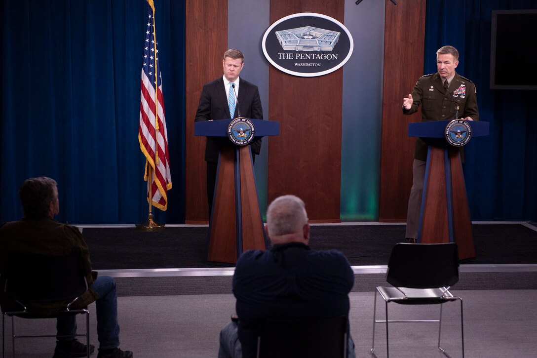 Two men stand next to each other on a podium and speak.