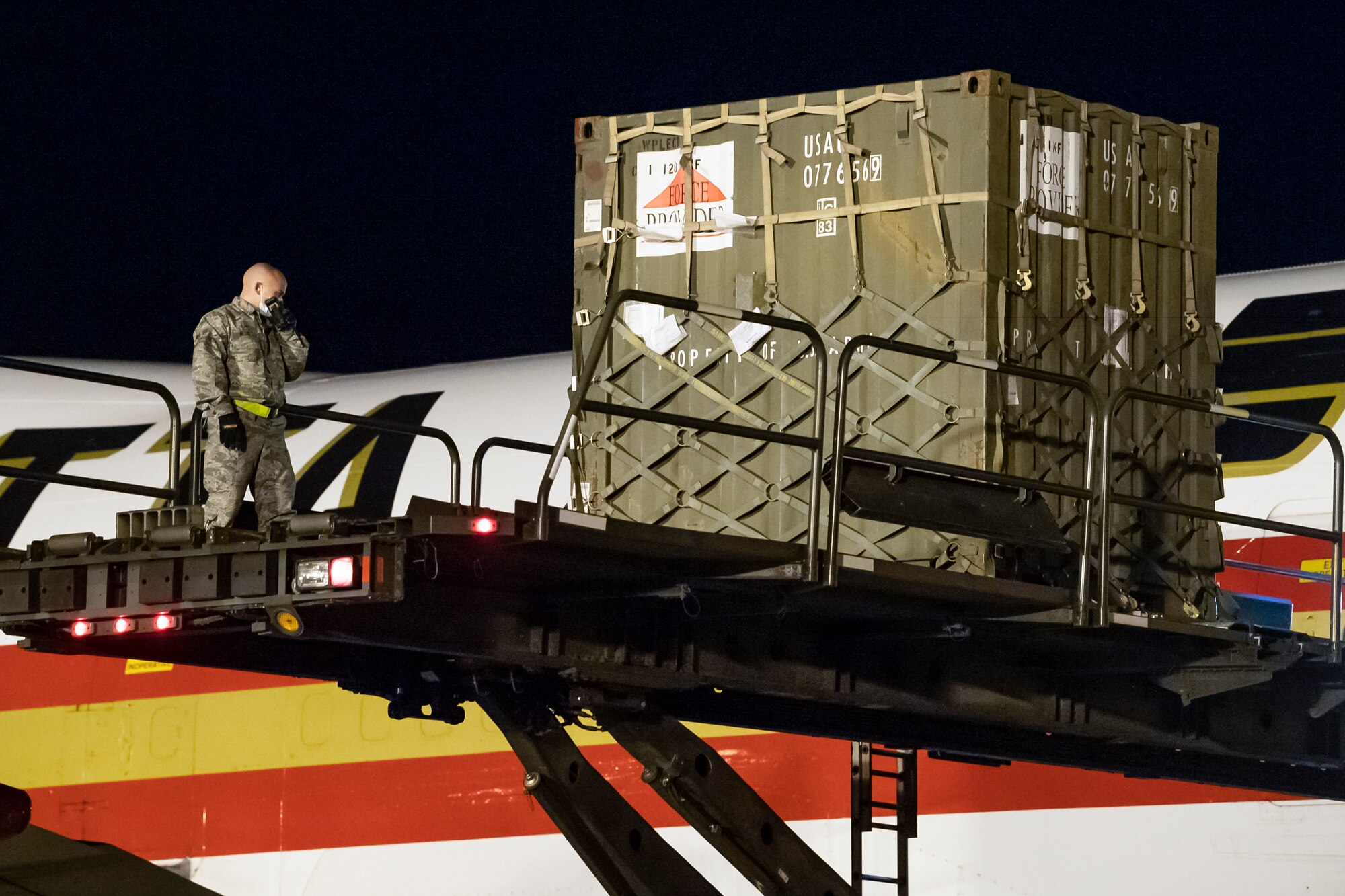Airman 1st Class Jacob Wilcox, 436th Aerial Port Squadron ramp services technician, listens to walkie-talkie communications while unloading cargo at Dover Air Force Base, Delaware, April 9, 2020. The technicians wear gloves and masks while loading and unloading cargo to combat COVID-19. (U.S. Air Force photo by Senior Airman Christopher Quail)