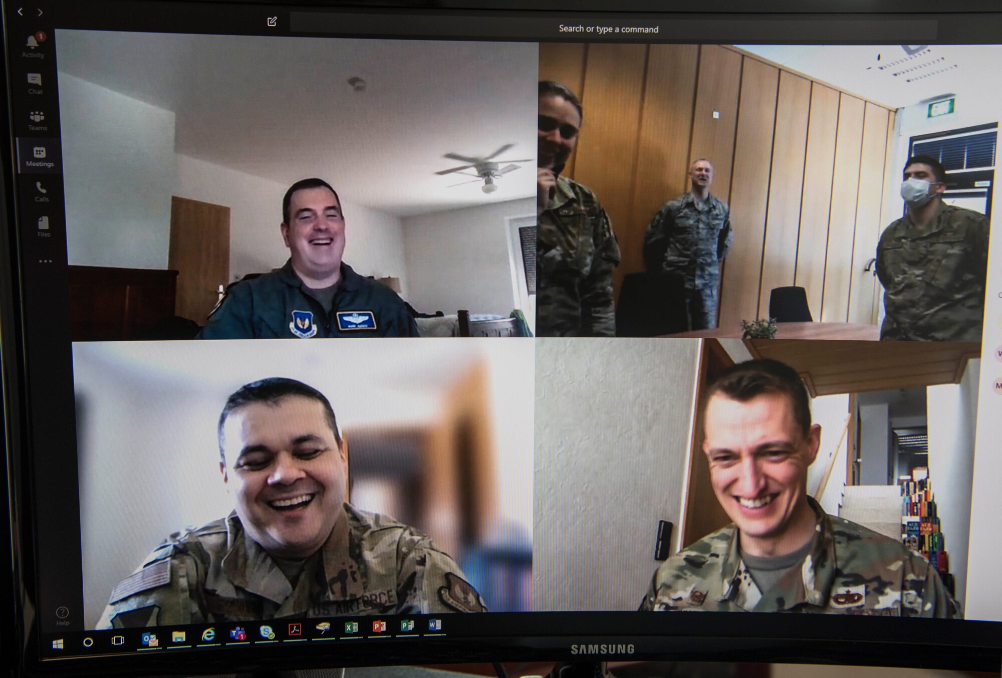 A computer monitor with four split screens shows six Airmen speaking to each other via teleconference video call.