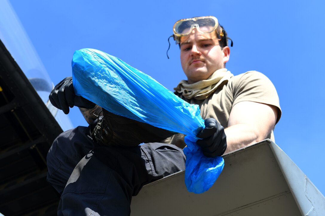 A 493rd Aircraft Maintenance Unit crew chief dons boot-covers as a precaution before sanitizing an F-15C Eagle cockpit to prevent the spread of COVID-19 at Royal Air Force Lakenheath, England, April 15, 2020. Personal protective equipment for cleaning includes wearing gloves, goggles and foot protection while using a sanitizing solution spray and cloth. Afterwards, each item is properly disposed of before the Airman returns to the squadron. (U.S. Air Force photo by Senior Airman Christopher S. Sparks)