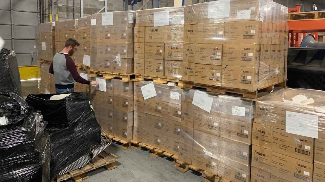 A warehouse worker inspects wrapped pallets of N95 mask boxes