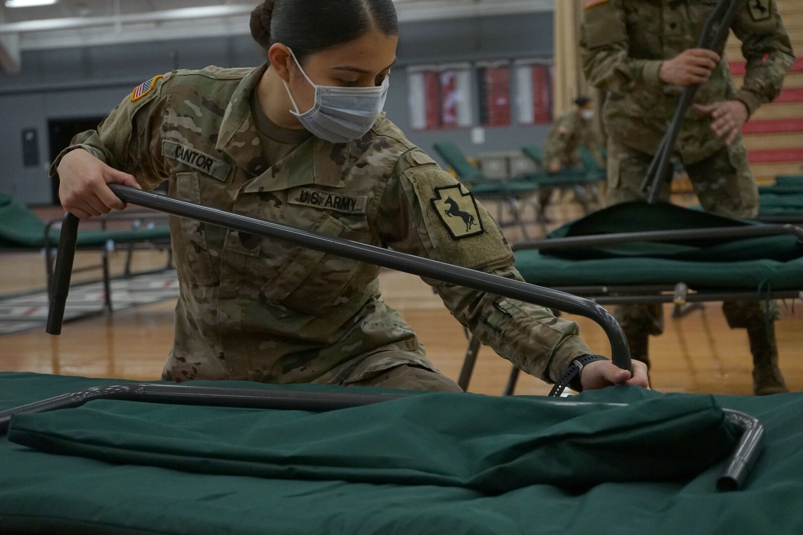 A Soldier from the Pennsylvania National Guard attaches the handrail of a cot during set up of an alternate care site at East Stroudsburg University's Koehler Fieldhouse, East Stroudsburg, Pa., April 14, 2020.