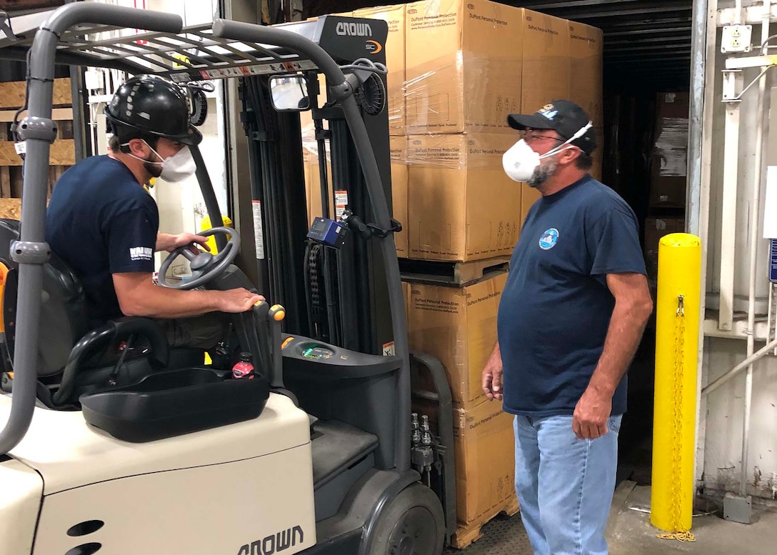 Andy McElroy, a transportation driver at Marine Corps Logistics Command, helps Shipping and Receiving Technician Christopher Leymeister (seated on forklift) with the loading of personal protective suits the command provided to the Defense Logistics Agency as part of their effort to gather supplies for the COVID-19 response.