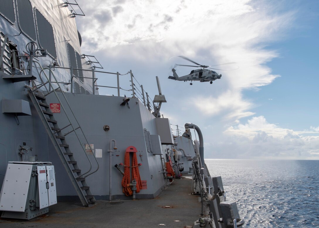 A helicopter flies over a U.S. Navy ship.