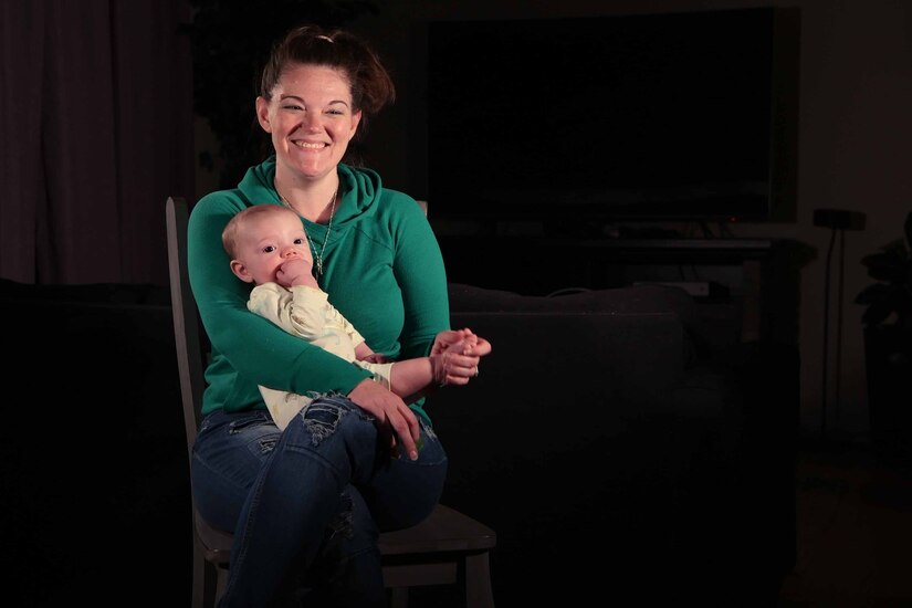 A smiling woman sits in a chair with a baby on her lap.