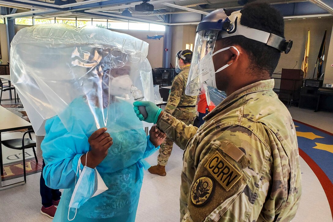 A service member administers a fit test on a face mask worn by another service member in medical scrubs.