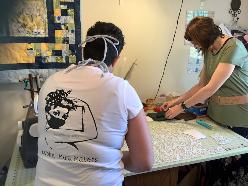 Photo shows both women working on a table to sew masks together.