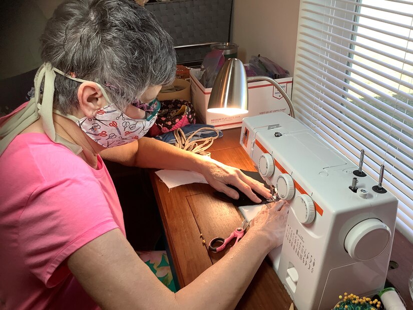 Photo shows Glenda Jackson sitting at a table working her sewing machine.