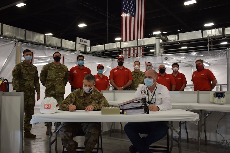 Col. Andrew Kelly, commander of the Jacksonville District of the U.S. Army Corps of Engineers, signs the letter certifying the completion of the Alternate Care Facility the district built in the Miami Convention Center as Kevin Guthrie, Deputy Director of the Florida Division of Emergency Management watches. The facility provides 450 beds, 50 of them intensive care unit beds, gives the state of Florida medical providers and state emergency managers flexibility as they prepare for a COVID-19 based surge at local and regional medical facilities. Initially, the facility was to be completed by April 27, but the deadline was moved to April 20 after a meeting with the Florida governor identified an expedited need. Even with the shortened deadline, the Corps of Engineers delivered the site early, with the contractor completing construction April 18 and the Corps signing over the facility to the state on April 19.