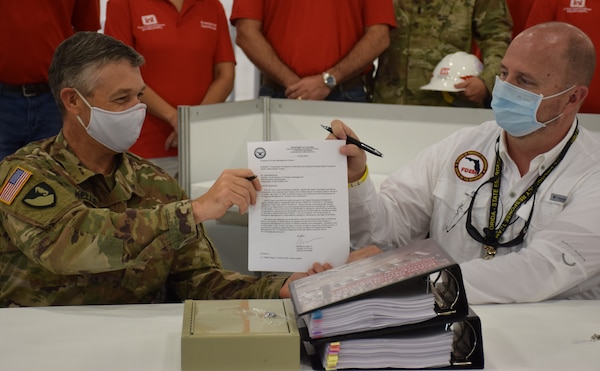 Col. Andrew Kelly, commander of the Jacksonville District of the U.S. Army Corps of Engineers, hands a letter certifying the completion of the Alternate Care Facility the district built in the Miami Convention Center to Kevin Guthrie, Deputy Director of the Florida Division of Emergency Management. The facility provides 450 beds, 50 of them intensive care unit beds, gives the state of Florida medical providers and state emergency managers flexibility as they prepare for a COVID-19 based surge at local and regional medical facilities. Initially, the facility was to be completed by April 27, but the deadline was moved to April 20 after a meeting with the Florida governor identified an expedited need. Even with the shortened deadline, the Corps of Engineers delivered the site early, with the contractor completing construction April 18 and the Corps signing over the facility to the state on April 19.