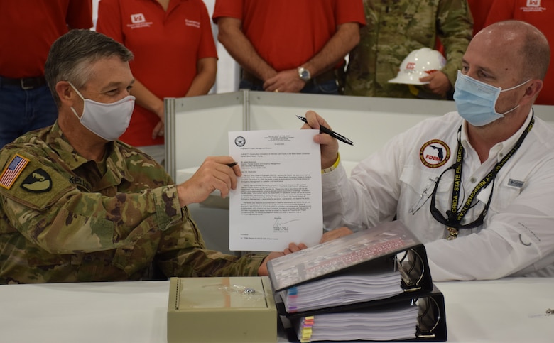 Col. Andrew Kelly, commander of the Jacksonville District of the U.S. Army Corps of Engineers, hands a letter certifying the completion of the Alternate Care Facility the district built in the Miami Convention Center to Kevin Guthrie, Deputy Director of the Florida Division of Emergency Management. The facility provides 450 beds, 50 of them intensive care unit beds, gives the state of Florida medical providers and state emergency managers flexibility as they prepare for a COVID-19 based surge at local and regional medical facilities. Initially, the facility was to be completed by April 27, but the deadline was moved to April 20 after a meeting with the Florida governor identified an expedited need. Even with the shortened deadline, the Corps of Engineers delivered the site early, with the contractor completing construction April 18 and the Corps signing over the facility to the state on April 19.