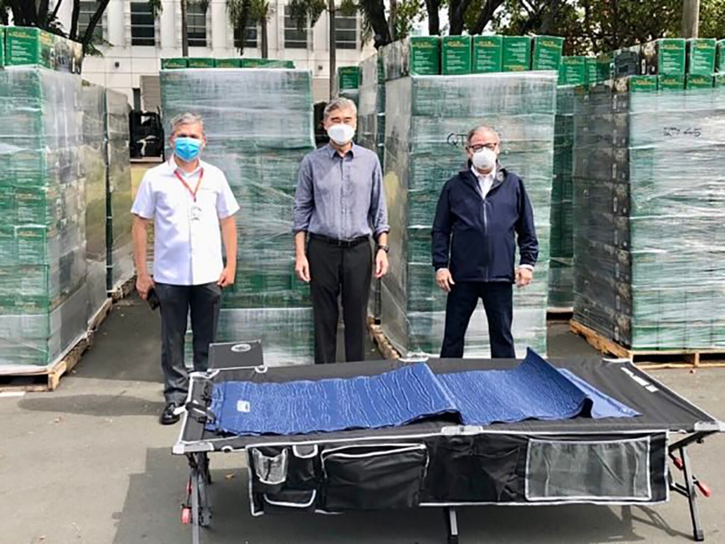 Government leaders pose in front of boxes of cots.