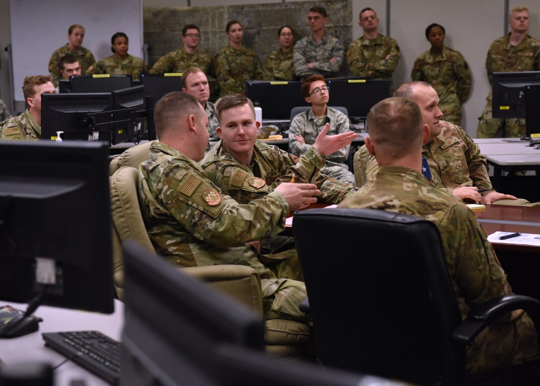U.S. Air Force Staff Sgt. Benjamin Bowers, 315th Training Squadron integrated operations exercise instructor supervisor, discusses the briefer’s content during Operation Lonestar, the capstone project for the four pipeline intelligence analyst students, in the 313th Training Squadron schoolhouse, on Goodfellow Air Force Base, Texas, March 5, 2020.  Bowers is one of nine course instructors who train the integrated environment by simulating an intelligence operations center. Note: This photo was taken before COVID-19 reached Goodfellow, the students and instructors are now practicing precautions and proper safety measures during the capstone. (U.S. Air Force photo by Airman 1st Class Abbey Rieves)