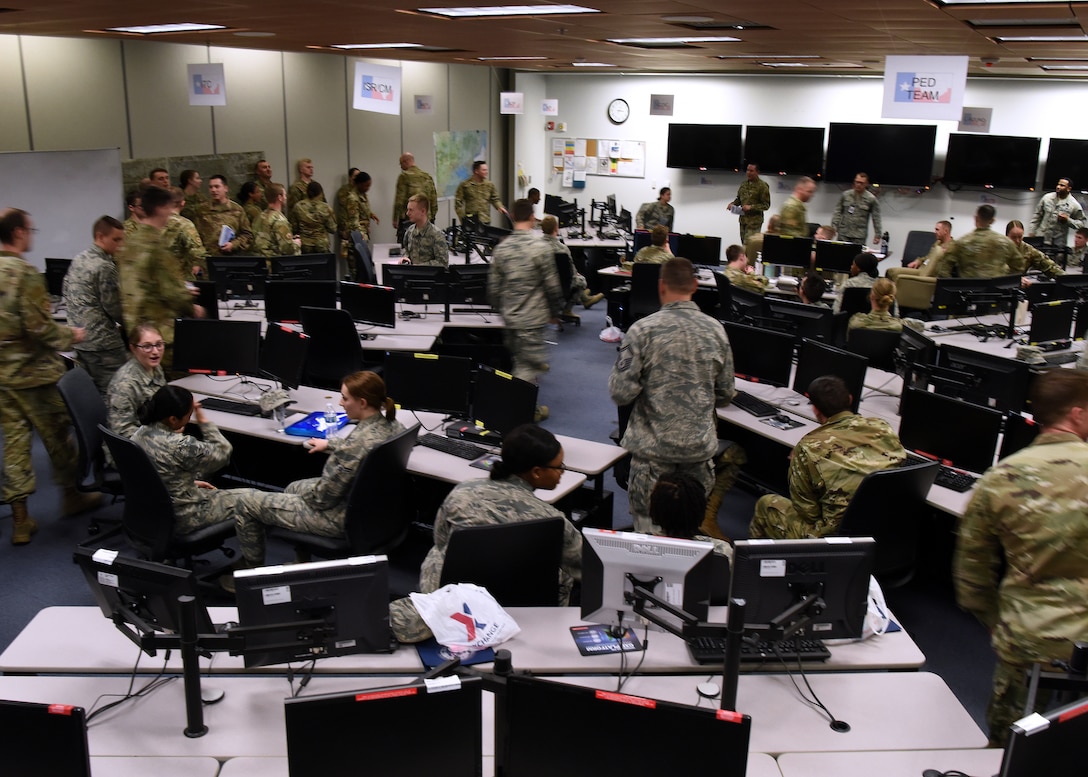 U.S. Air Force students from the 315th Training Squadron hustle around the classroom during Operation Lonestar, the capstone project for the four pipeline intelligence analyst students, in the 313th Training Squadron schoolhouse, on Goodfellow Air Force Base, Texas, March 5, 2020. The students base their analysis on thousands of simulated signals and intelligence reports with fully integrated full-motion videos representing a common operating picture during their pipeline training in a mock intelligence operations center. Note: This photo was taken before COVID-19 reached Goodfellow, the students and instructors are now practicing precautions and proper safety measures during the capstone. (U.S. Air Force photo by Airman 1st Class Abbey Rieves)