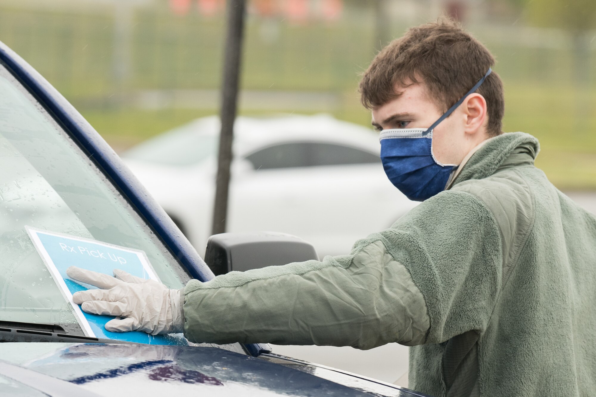 Airman 1st Class Jacob Goucher, 436th Aircraft Maintenance Squadron C-5M apprentice, places a number card on a vehicle windshield at a curbside pharmacy, April 18, 2020, at Dover Air Force Base, Delaware. The curbside project offers full pharmacy services including new prescriptions and refills, allowing Team Dover to access prescriptions and maintain social distancing. (U.S. Air Force photo by Mauricio Campino)