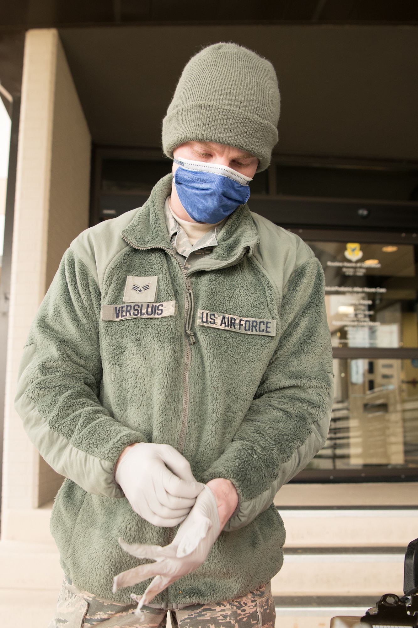 Senior Airman Landon Versluis, 436th Maintenance Squadron structural mechanic, dons latex gloves and a mask at the start of his shift for the curbside pharmacy, April 18, 2020, at Dover Air Force Base, Delaware. The curbside project offers full pharmacy services including new prescriptions and refills, allowing Team Dover to access prescriptions and maintain social distancing. (U.S. Air Force photo by Mauricio Campino)