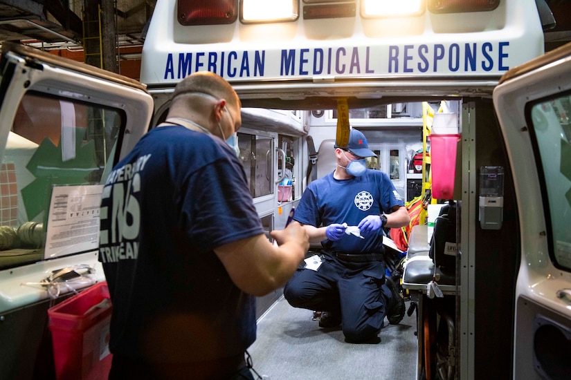 Medical technicians wearing protective gear sanitize the inside of an ambulance.